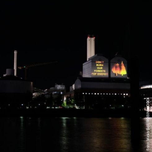 Das Heizkraftwek Tiefstack in Hamburg im Dunkeln. Auf die Fassade wird mit Licht der Satz "Don't burn our forests for energy" und daneben zwei brennende Bäume projiziert. 